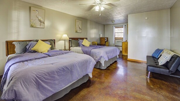 A hotel room with two beds, a ceiling fan, a sofa, and artwork on the walls.