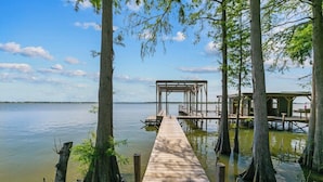 Une jetée en bois menant à un quai doté d’un espace de repos abrité, le tout entouré d’arbres et bordé par une étendue d’eau calme.