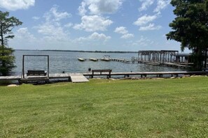 A grassy area with a wooden dock extending into a body of water, a swing set, and a bench.