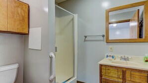 A bathroom with a toilet, a shower with a glass door, a sink with a mirror, and wooden cabinets.