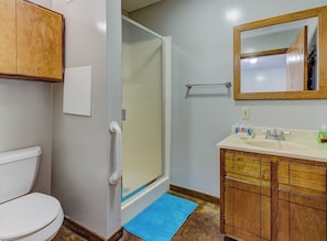 A bathroom with a toilet, a shower with a glass door, a sink with a mirror, and wooden cabinets.