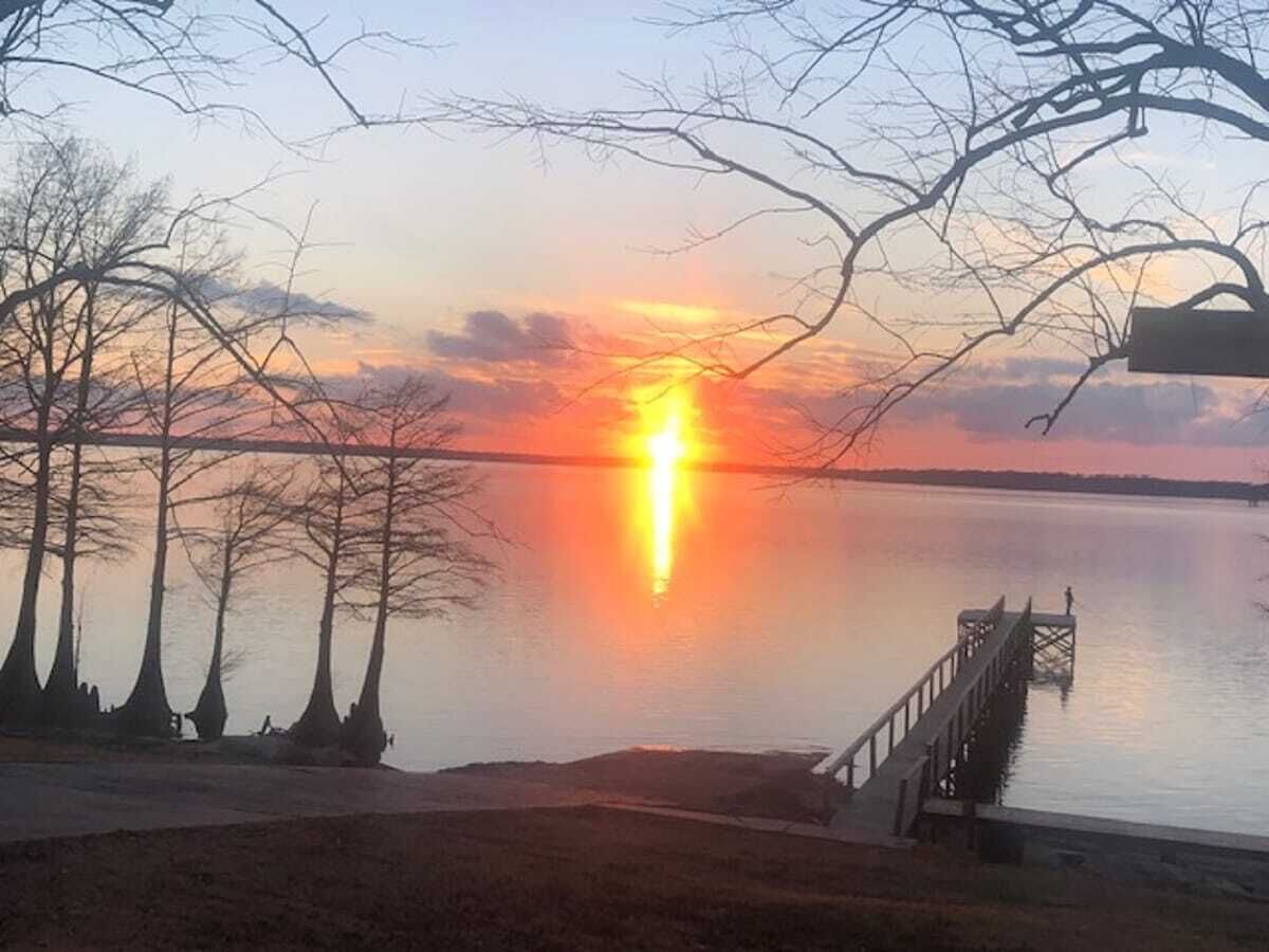 Un coucher de soleil sur un lac paisible, avec une jetée qui s’avance dans l’eau.