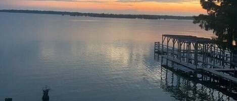 A calm lake at sunset with a dock and grassy area.