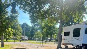 A campground with RVs, trees, and a gravel path. - Sunset View RV Spot 30 AMP (Vicksburg)