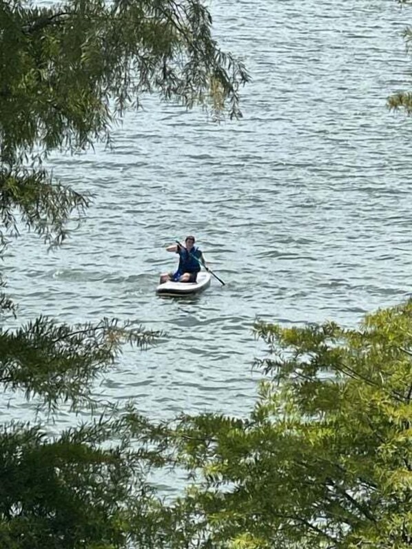 A person paddling a small boat on a body of water surrounded by trees.