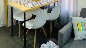 Een eetgedeelte met een tafel, stoelen, een plafondlamp, gordijnen en een bank met een kussen.