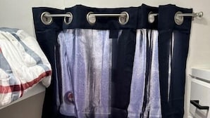 Une petite pièce avec un lit, une bouche d’aération et un rideau.