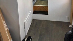 Un couloir étroit avec un plancher en bois, un radiateur et une porte donnant sur une pièce où se trouvent un lit et un rideau.