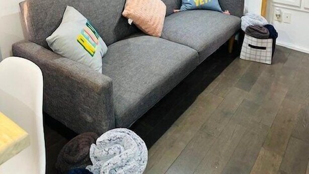 Een woonkamer met een bank, kussens, een klein tafeltje en een televisie aan de muur.