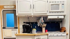 Une cuisine compacte avec des meubles blancs, un four à micro-ondes, une cuisinière et une machine à café.