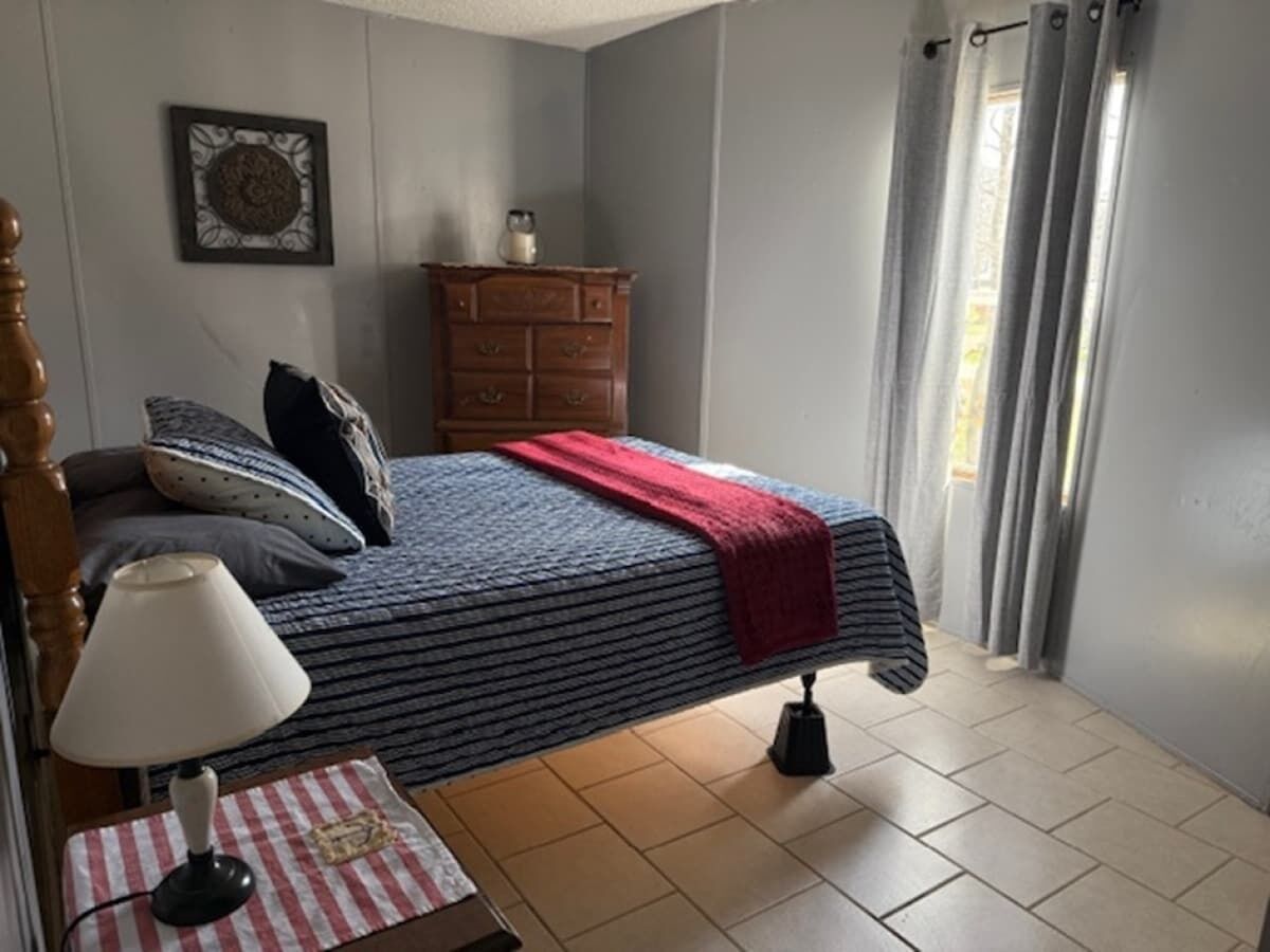 A bedroom with a bed, a dresser, a lamp, and a window with curtains.