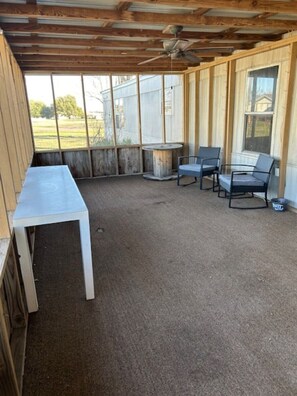 A covered patio area with a table and chairs, a ceiling fan, and a view of a house through large windows.