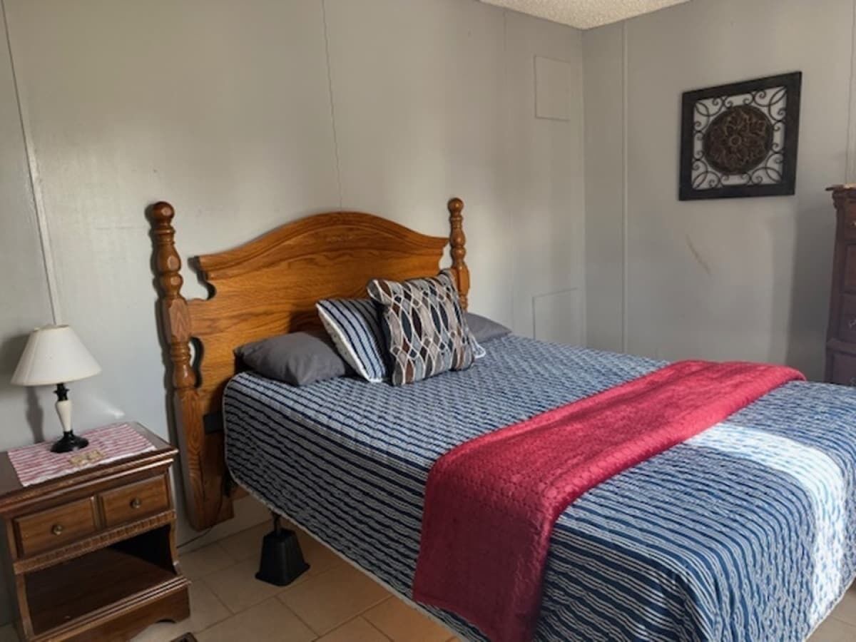 A bedroom with a wooden bed, a nightstand, a lamp, and a decorative wall piece.