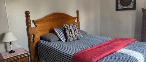 A bedroom with a wooden bed, a nightstand, a lamp, and a decorative wall piece.