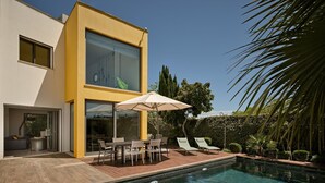 Ein modernes Haus mit Schwimmbad, Gartenmöbeln und einer Terrassenfläche.