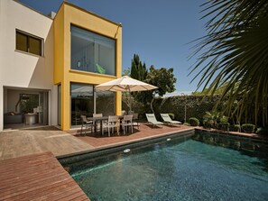Een modern huis met een zwembad, tuinmeubilair en een terras.
