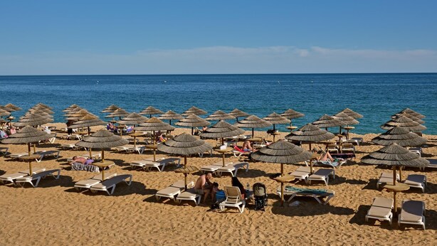 Ein Strand mit Reihen von Liegestühlen und Reetsonnenhüten.