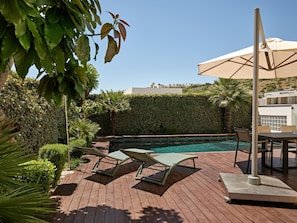 A wooden deck with a pool, lounge chairs, and an umbrella.