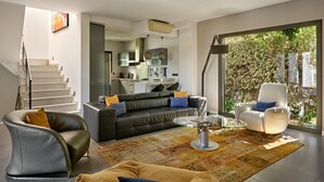 Ein modernes Wohnzimmer mit Sofa, Sessel und Couchtisch, einer Treppe und einer Küche im Hintergrund.