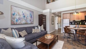 A spacious living room with a gray sofa, a coffee table, and a large abstract painting on the wall.