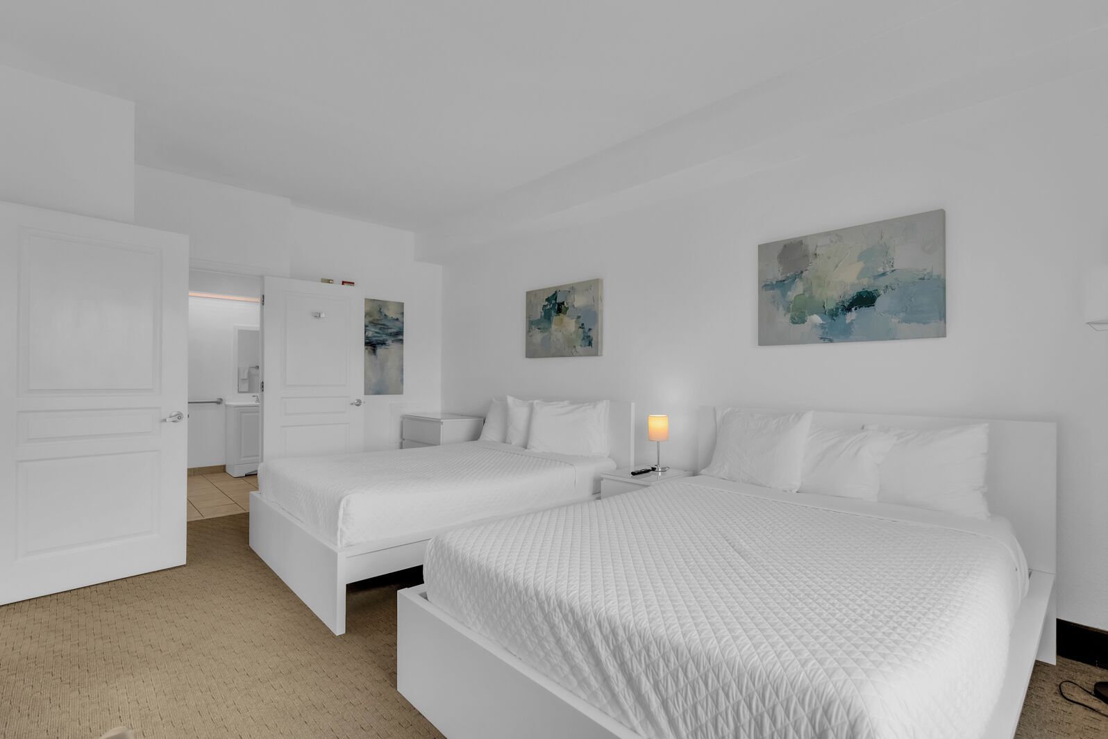 A white room with two beds, a nightstand, and abstract art on the walls.