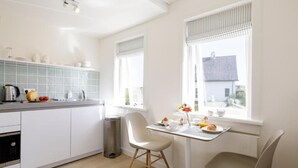 A modern kitchen with white cabinets, a stainless steel sink, and a dining area with two chairs and a table. - Villa Parnassia (Bergen aan Zee)