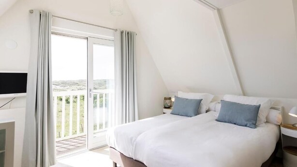 A bedroom with a large bed, a TV, and a balcony with curtains. - Villa Parnassia (Bergen aan Zee)
