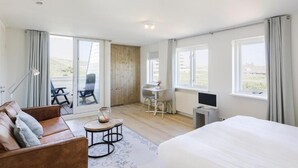 A modern hotel room with a large bed, a sofa, a desk with a computer, and a balcony with chairs. - Villa Parnassia (Bergen aan Zee)
