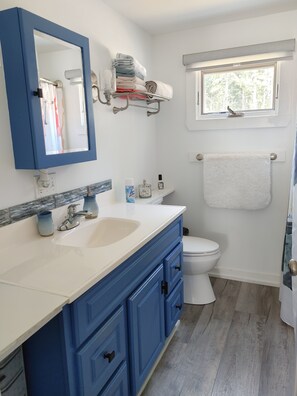 A bathroom with a white sink, blue vanity, and a toilet. There is a window above the toilet and a towel rack with towels.