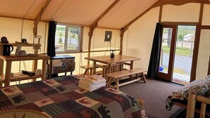 A tented room with a bed, a table, and a bench. There is a window and a door leading outside. - Howling Wolf Resort!  (Seward)
