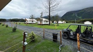 A view of a campsite with several cabins, a jeep, and a mountainous landscape. - Howling Wolf Resort!  (Seward)