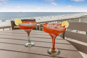 Kaksi cocktail-drinkkiä puisella pöydällä, josta avautuu näkymä rannalle.