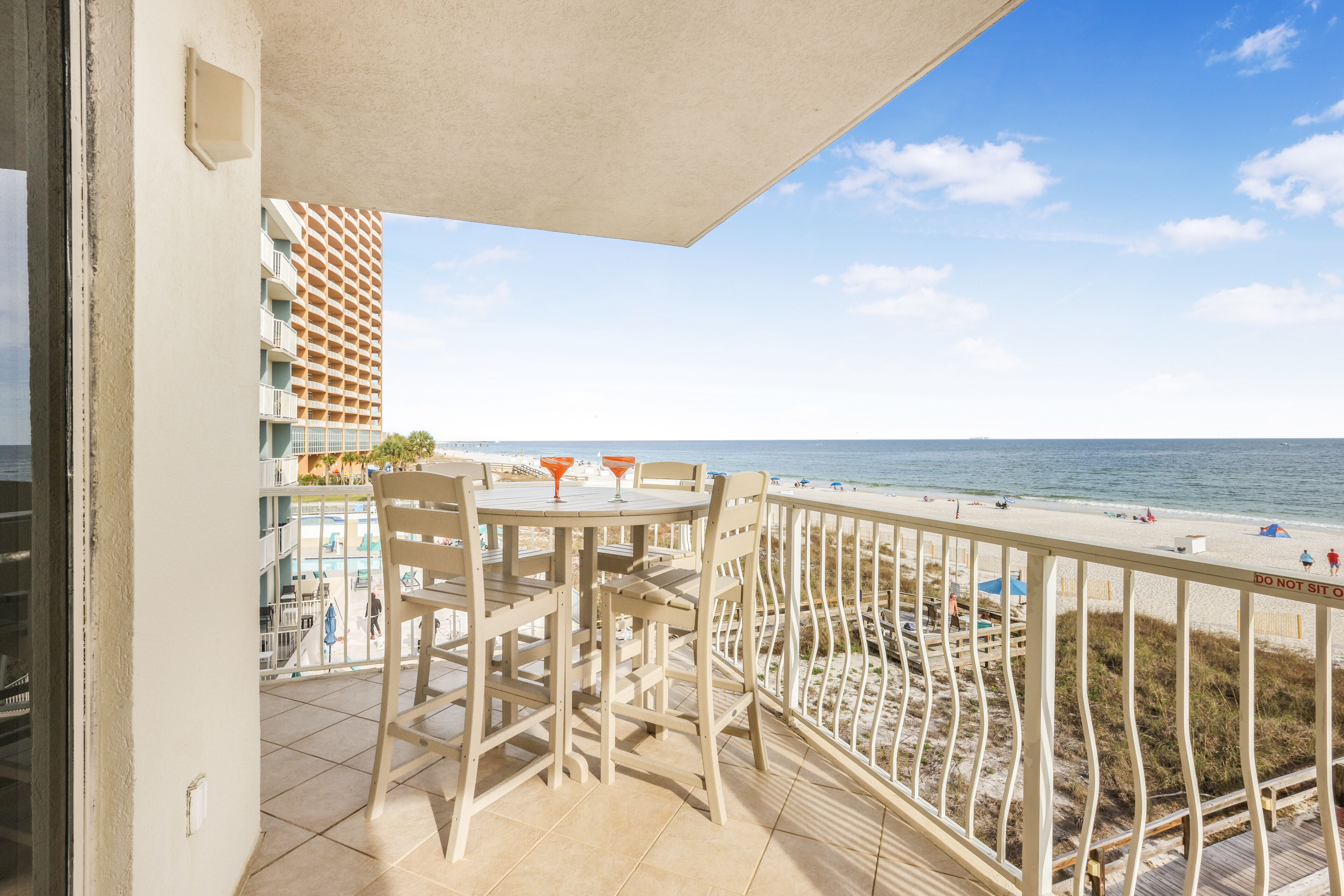 A balcony with a view of the beach, a table with chairs, and a railing.