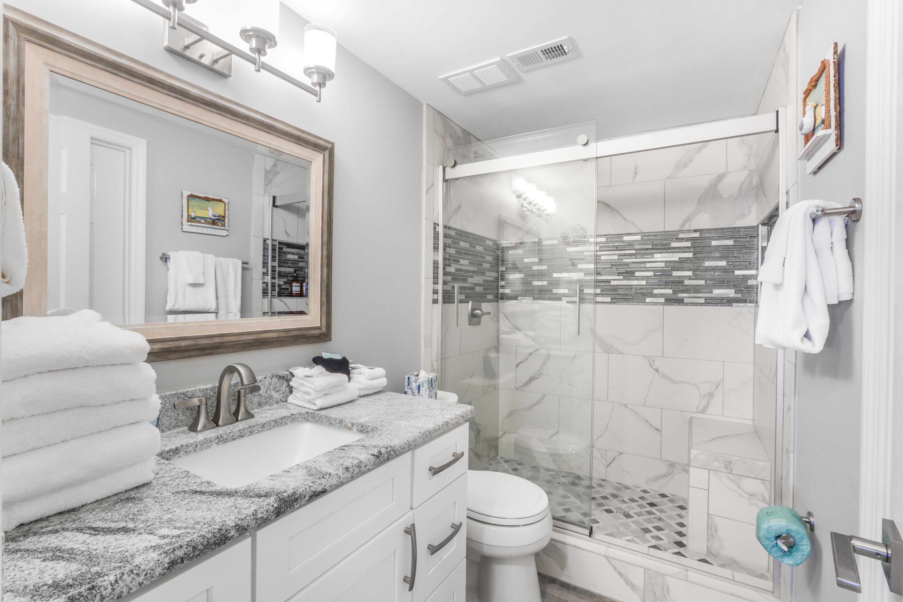 Une salle de bain moderne avec un lavabo surmonté d’un plan de travail en granit, un grand miroir, une douche en verre et des toilettes.