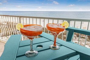 Dois cocktails sobre uma mesa azul-turquesa, com vista para a praia e o oceano.