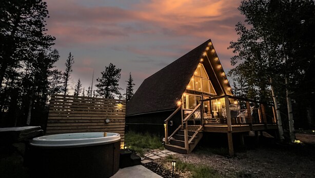 A wooden cabin with a thatched roof, a hot tub, and a deck with stairs leading to the entrance.