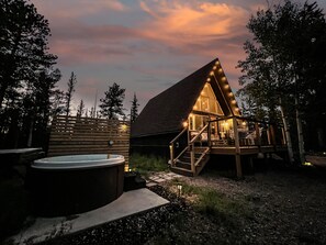 En stuga byggd av trä med ett halmtak, ett bubbelbad och en terrass med en trappa som leder till entrén.