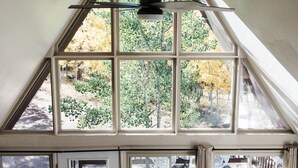 A room with a sloped ceiling, large windows, a door with a view, a brown leather chair, and a floor lamp.