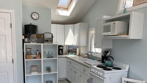A compact kitchen with white cabinets, a stove, a microwave, and a small window.