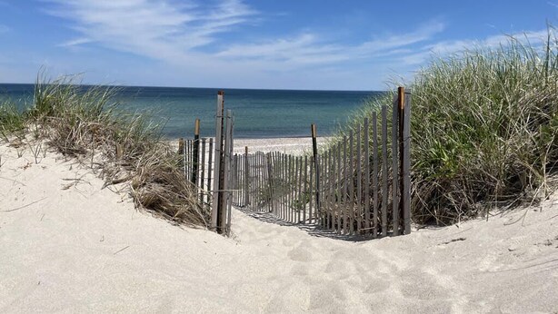 A sandy beach with a wooden fence leading to the water.