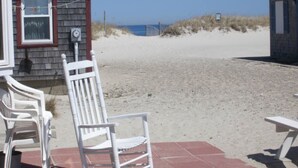 A beachside building with a red-tiled patio, white plastic chairs, and a view of the beach and ocean.