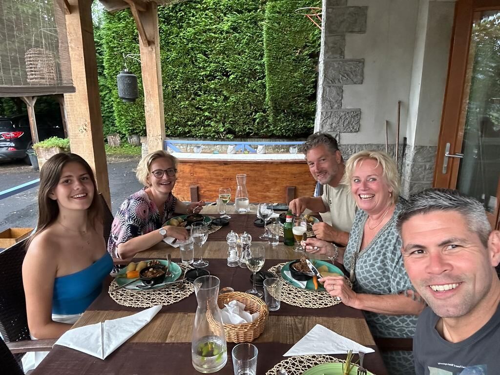 A group of people dining at an outdoor table with a view of greenery.
