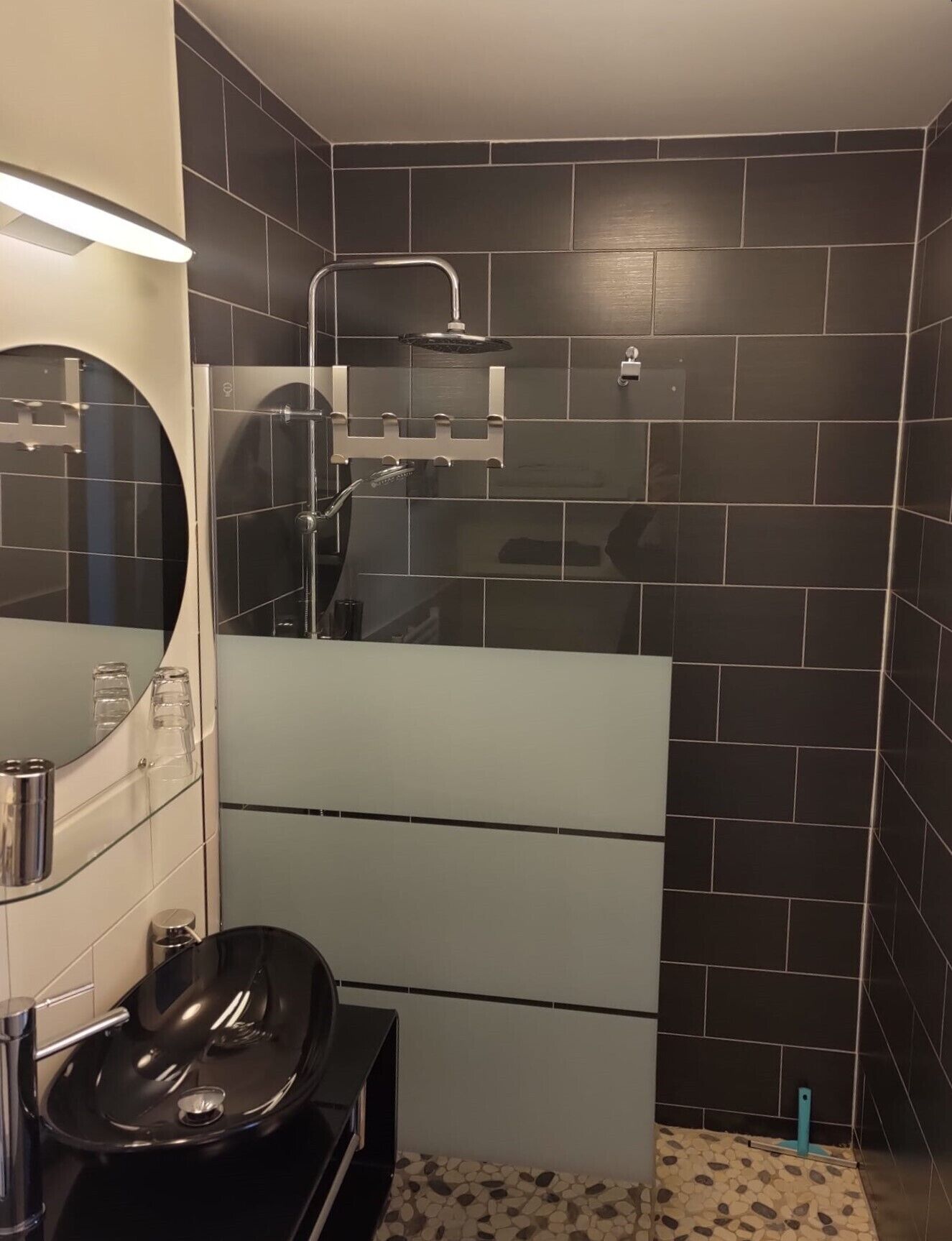 A modern bathroom with a black tiled shower, a glass sink, and a mirror.