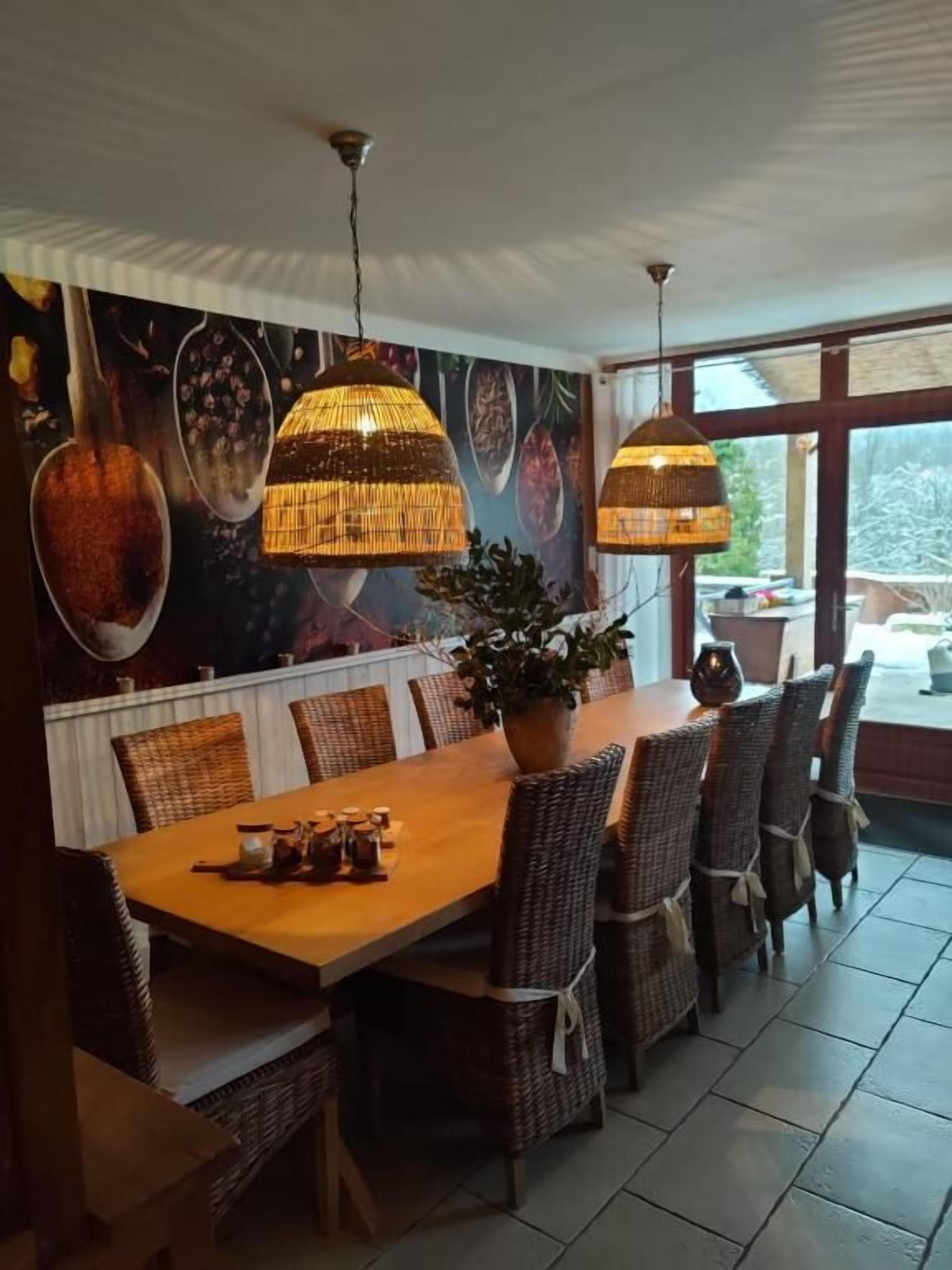 A dining area with a long wooden table, wicker chairs, and hanging wicker lamps.
