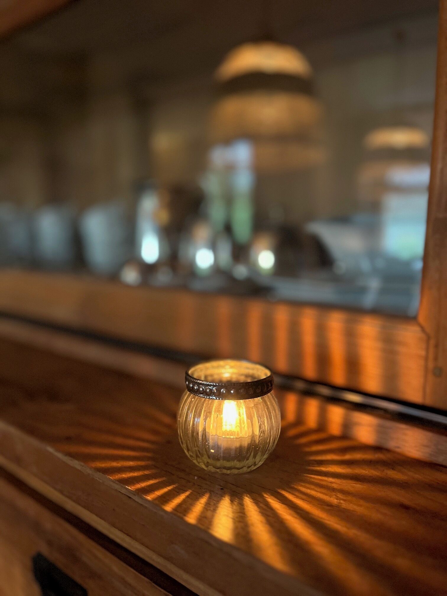 Una pequeña vela de vidrio transparente sobre una superficie de madera, reflejando un interior borroso.