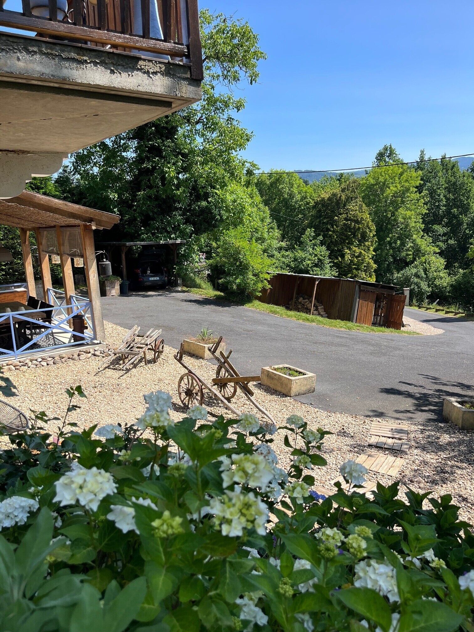 A rustic outdoor area with a wooden structure, a cart, and a gravel path.