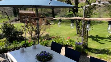 An outdoor dining area with a white table, a blue umbrella, and a garden view.