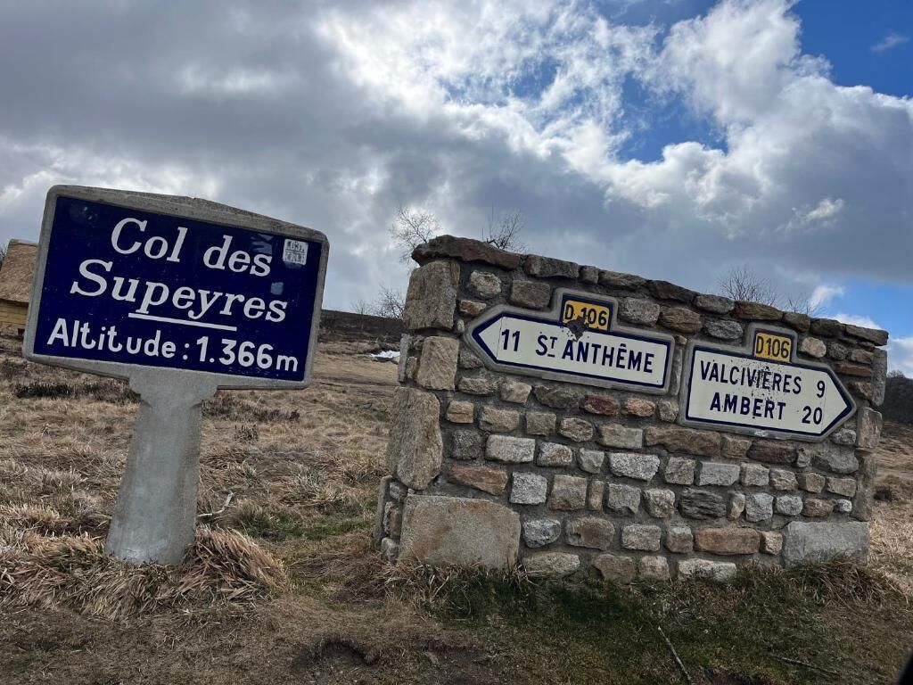 Un cartel con indicaciones hacia el Col des Supeyres, altitud 1.366m, y lugares cercanos como 11 St. Anthème, Valcivieres 9 y Ambert 20.
