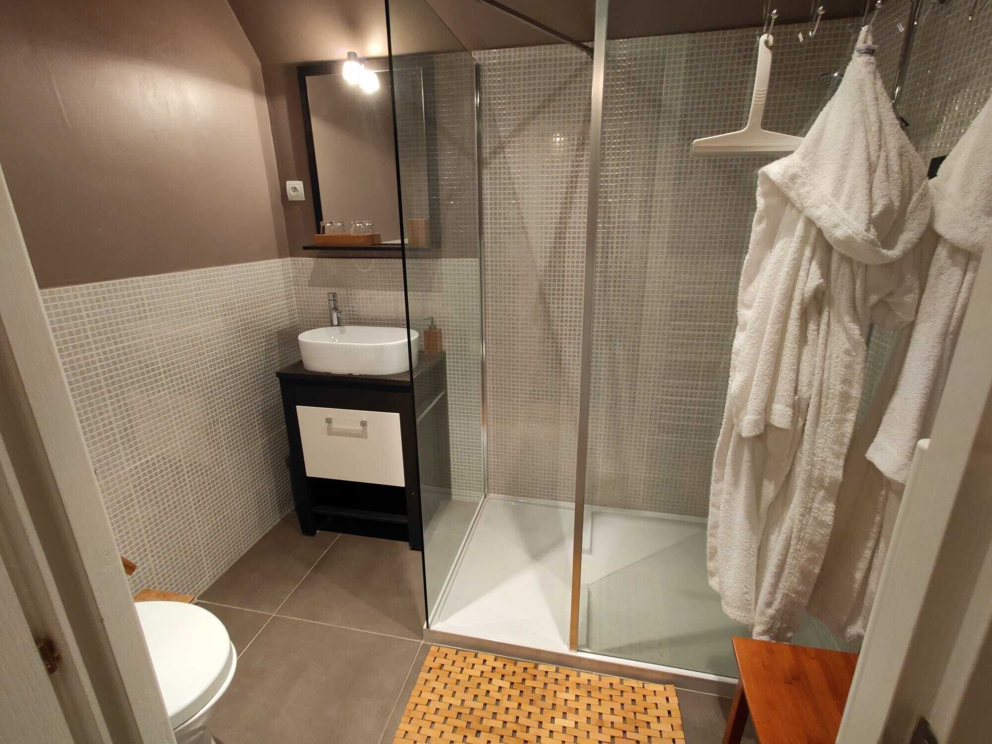 A modern bathroom with a glass shower enclosure, a white sink, and a wooden bath mat.