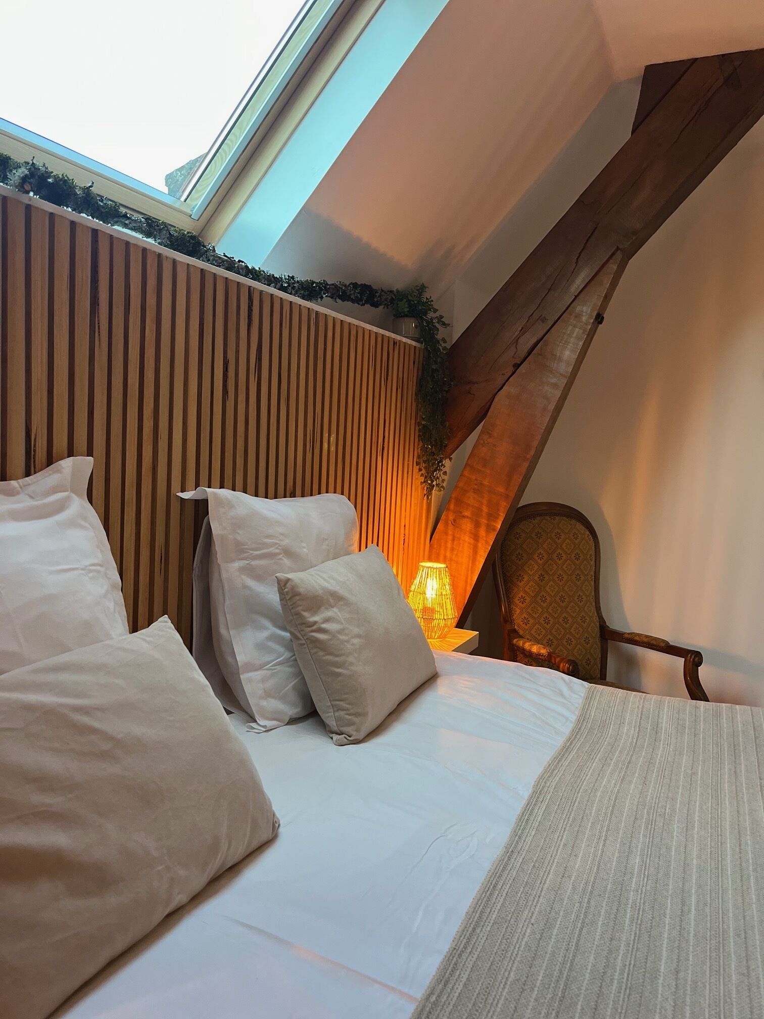 Une chambre avec un plafond en pente, un mur lambrissé et un lit recouvert de draps et d’oreillers blancs.